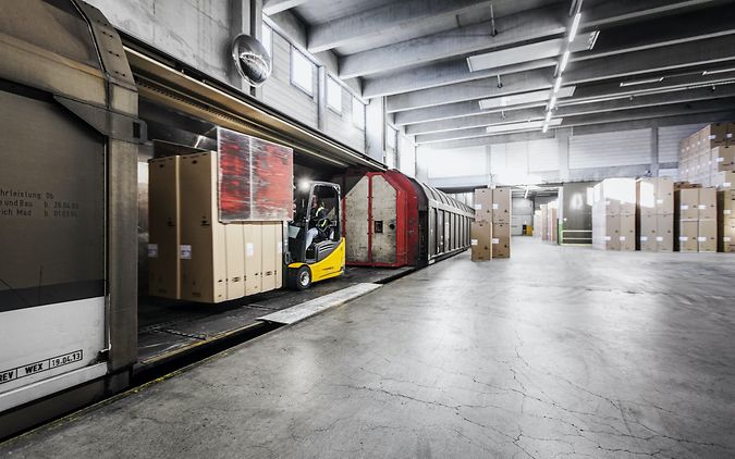 A forklift truck loads a freight wagon in a warehouse with a railway siding