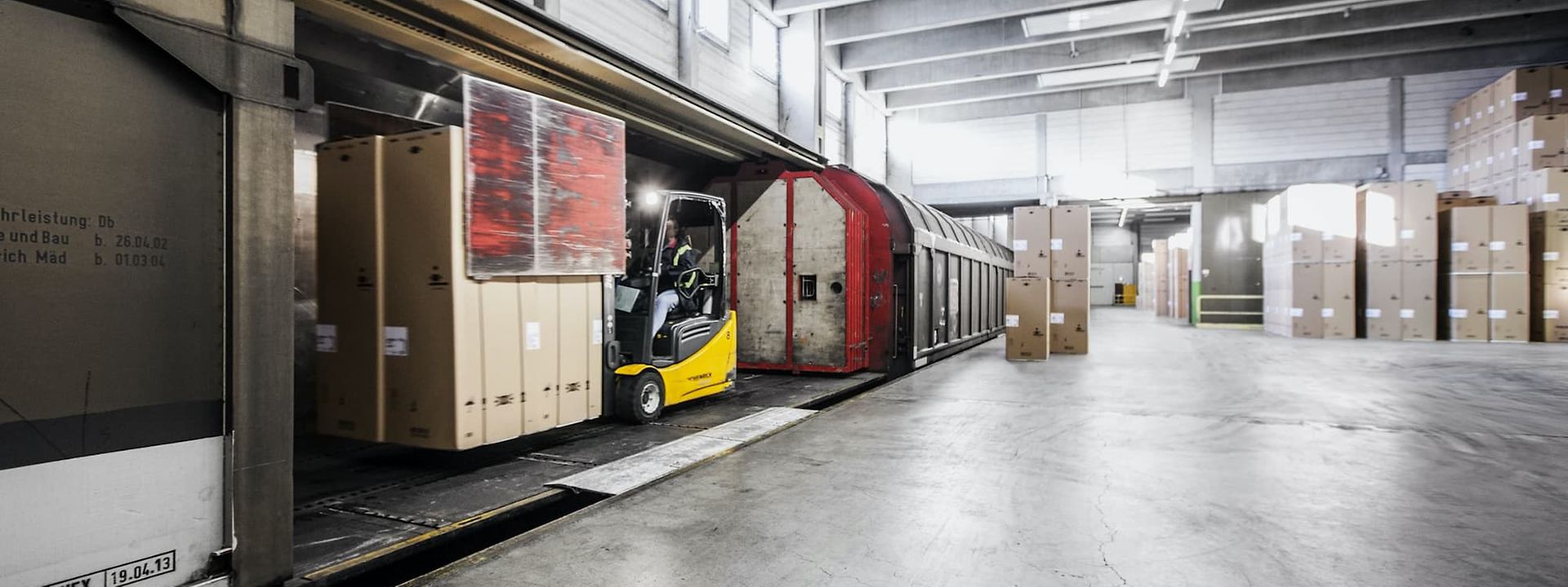 A forklift truck loads a freight wagon in a warehouse with a railway siding