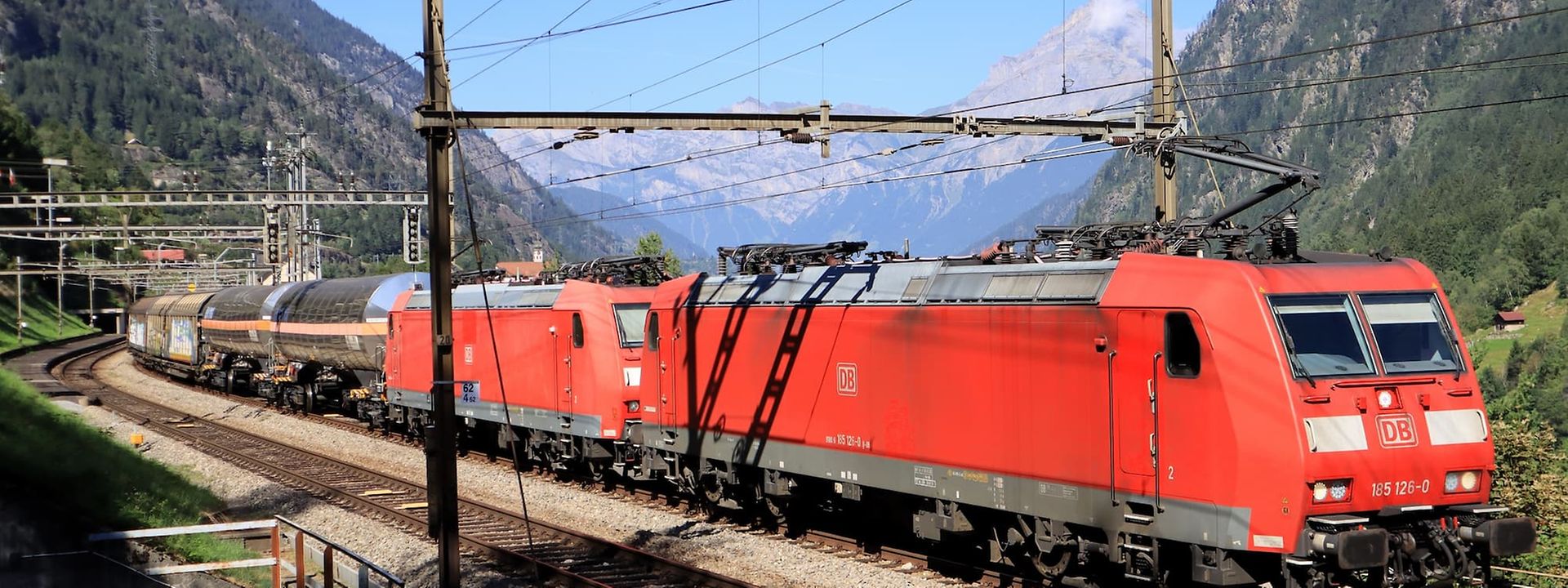 Red DB cargo trains on a curved mountain railway with breathtaking alpine views.